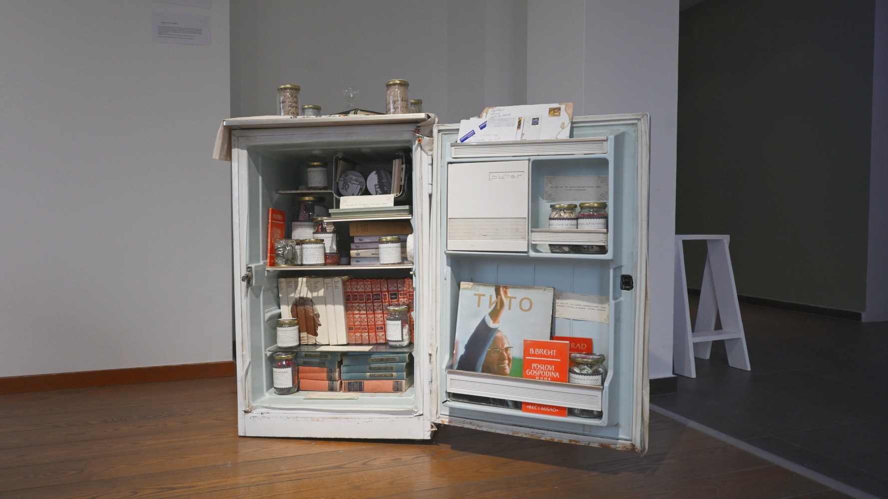 Фотографија од уметничка инсталација од фрижидер со стари книги и предмети 