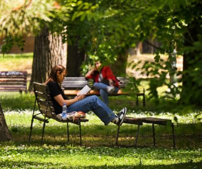 Фотографија од девојка која чита книга на клупа во парк